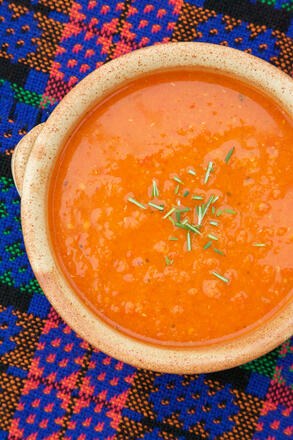 Gluten free roasted red pepper soup on blue mat with spoon