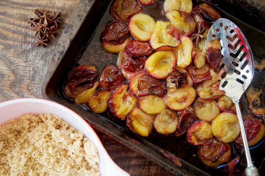 Roasted plum crumble bowl with stewed fruit and serving spoon